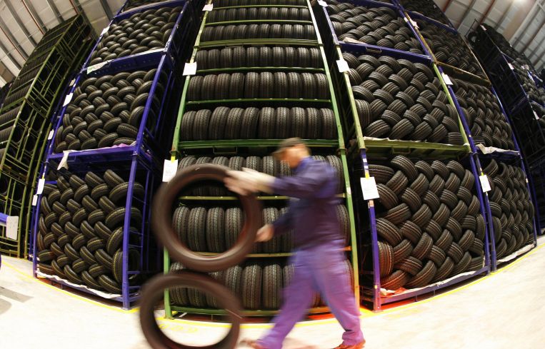 An employee rolls tires past a wall of tires.