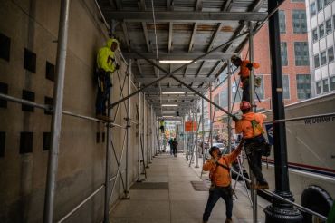 Construction workers erect scaffolding on a street in Manhattan.