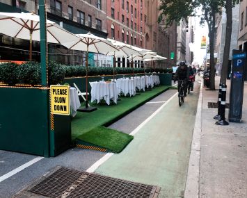 Outdoor Dining structure with Please Slow Down sign and bike lane filled with bike delivery people racing by, Manhattan, New York.
