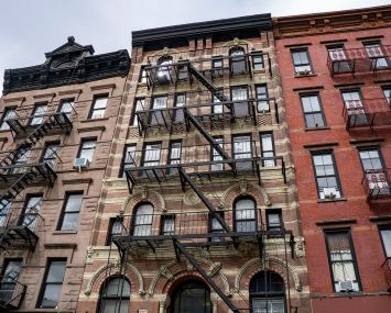 A set of narrow apartment buildings, each a few stories and with fire escapes running down them.
