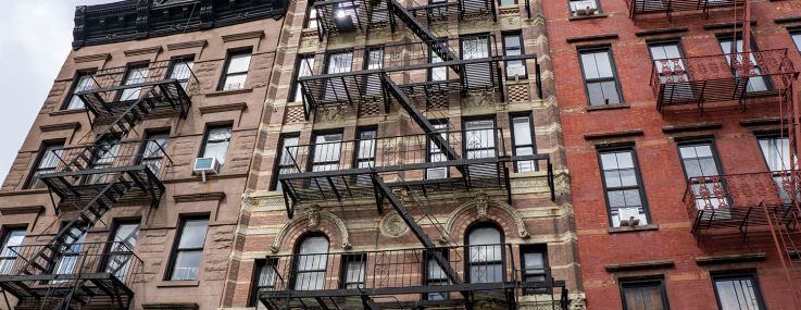 A set of narrow apartment buildings, each a few stories and with fire escapes running down them.
