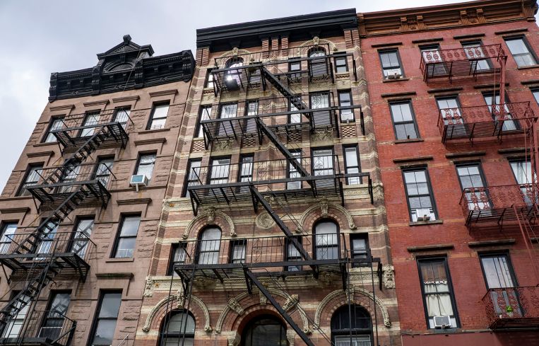 A set of narrow apartment buildings, each a few stories and with fire escapes running down them.