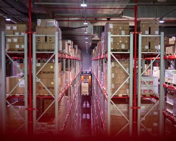 Employee carries a pallet on a forklift truck in an aisle of a warehouse.