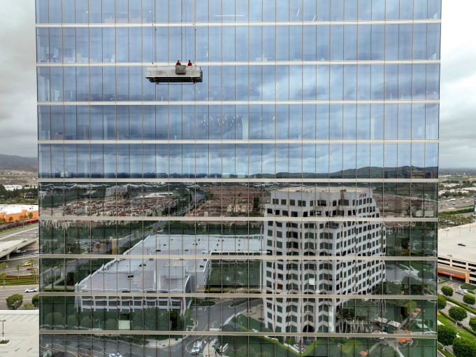 Window washers work on the upper floors of 400 Spectrum Center as buildings are reflected in the lower portion of the 20-story tower in Irvine.