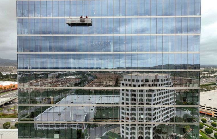 Window washers work on the upper floors of 400 Spectrum Center as buildings are reflected in the lower portion of the 20-story tower in Irvine.