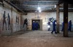 Tour attendees dressed in protective equipment pass by a series of painted figures on the walls of a former boxing gym in the basement of the armory.