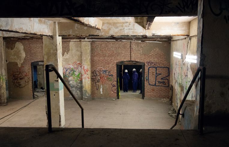 A staircase leading to a landing and a pair of double doors on the opposite wall of a large, windowless room.