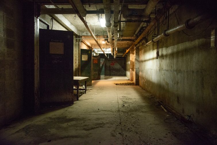 A long, dimly lit hallway with rusty pipes overhead.