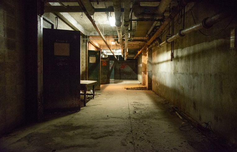 A long, dimly lit hallway with rusty pipes overhead.