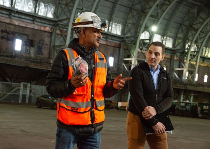 Two men speak to a tour group inside the historic drill hall of an armory in the Bronx.