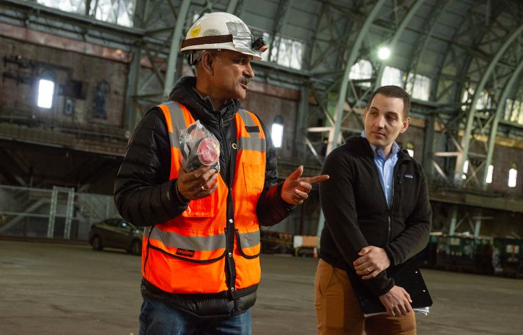 Two men speak to a tour group inside the historic drill hall of an armory in the Bronx.
