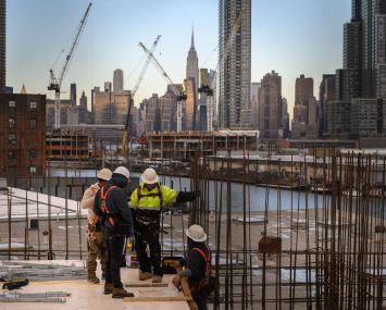 Four construction workers talk to each other with the Manhattan skyline in the background.