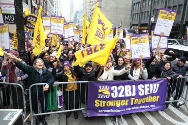 Union members wave yellow and purple signs behind a police barricade in Manhattan.