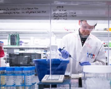 A scientist in a white coat uses a pipette in a lab.