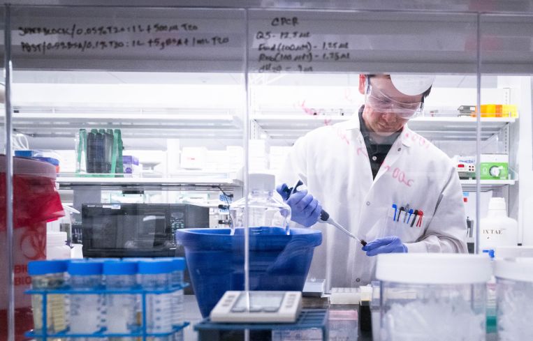 A scientist in a white coat uses a pipette in a lab.