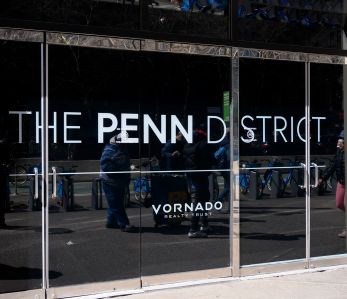 Pedestrians are reflected in the windows of one of Vornado's Penn District buildings.