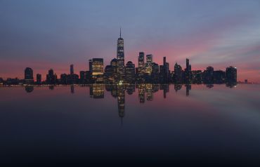 JERSEY CITY, NJ - JANUARY 6: The skyline of lower Manhattan and One World Trade Center is reflected on the top of a monument as the sun rises in New York City on January 6, 2024, as seen from Jersey City, New Jersey.  (Photo by Gary Hershorn/Getty Images)