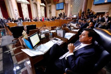 Former Los Angeles City Councilmember Jose Huizar, listens as speakers deliver arguments at Los Angeles City Hall. Former Councilman Mitch Englander sits behind him.