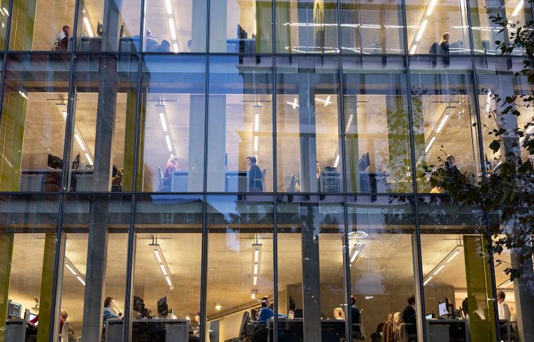 People working at their desks in an exterior night view of an office building.