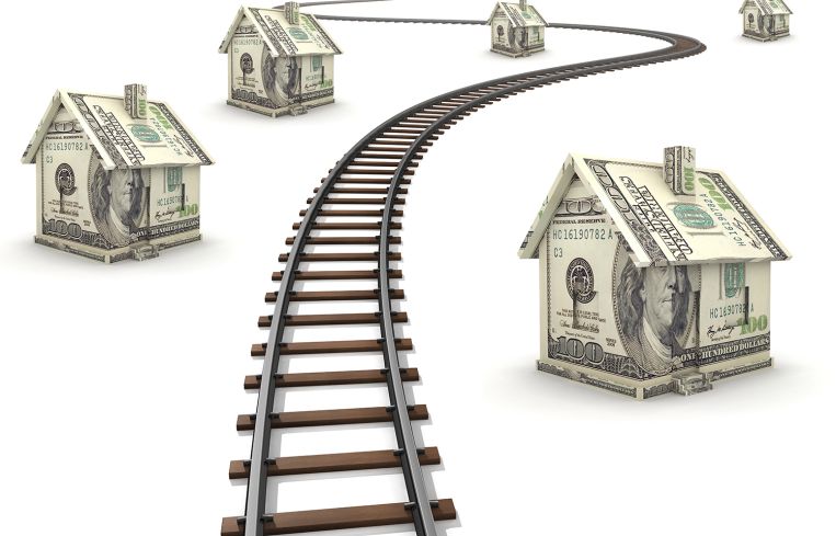 Railroad tracks running through houses made of money.