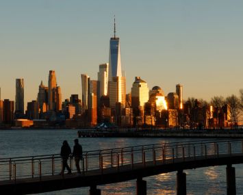 HOBOKEN, NJ - FEBRUARY 19: The sun sets on the skyline of lower Manhattan and One World Trade Center in New York City as people walk on a pier in the Hudson River on February 19, 2024, in Hoboken, New Jersey. (Photo by Gary Hershorn/Getty Images)