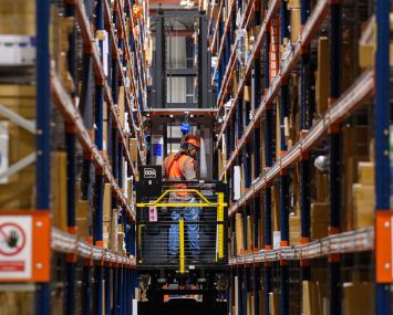 A forklift truck drives through high shelves inside a distribution center.
