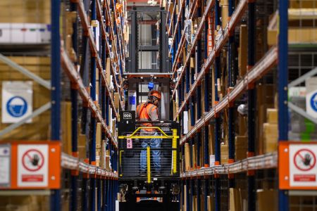 A forklift truck drives through high shelves inside a distribution center.
