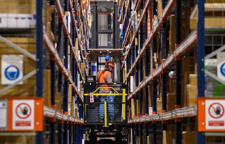 A forklift truck drives through high shelves inside a distribution center.