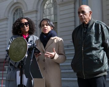 Three people at a podium on the steps of City Hall in Manhattan.