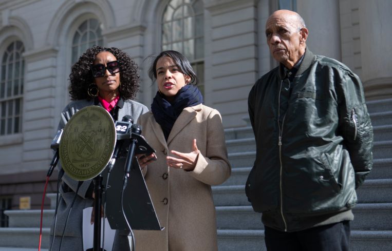 Three people at a podium on the steps of City Hall in Manhattan.