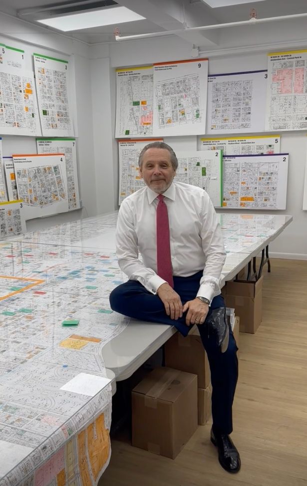 A man in a red tie sitting on a card table surrounded by maps.