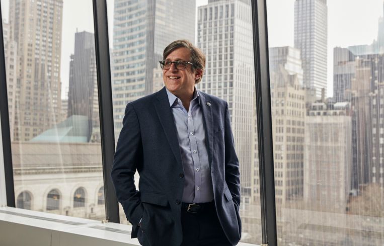 A man in glasses standing at a window.