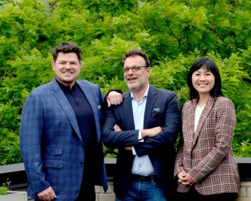 Three people in business attire standing in front of a grove of trees.