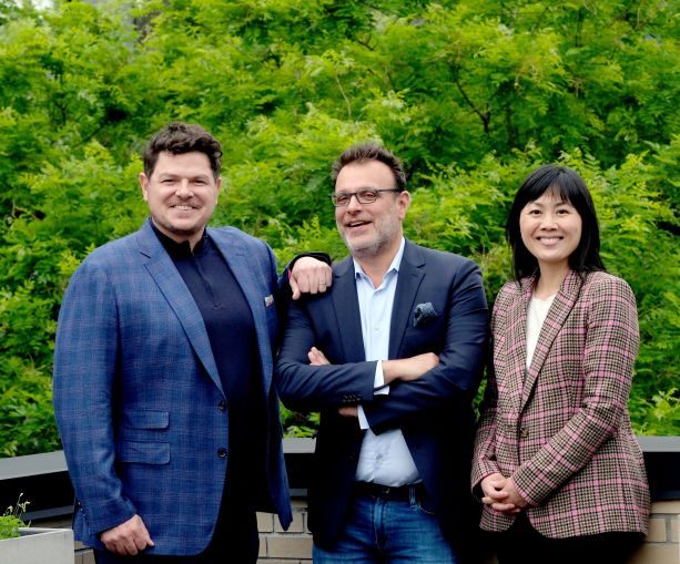 Three people in business attire standing in front of a grove of trees.