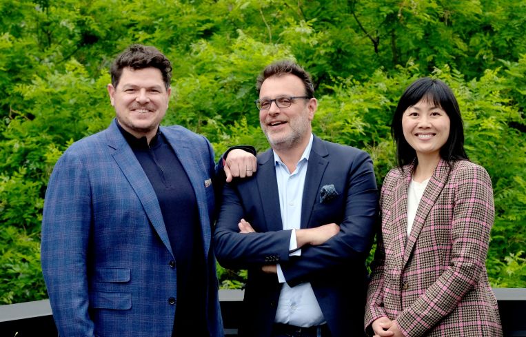 Three people in business attire standing in front of a grove of trees.