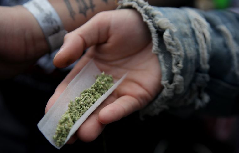 A person's hand holding a cannabis joint.