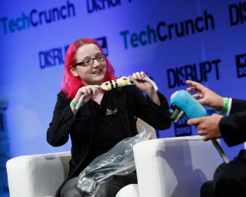 A woman with pink hair on a stage with a man holding an electronic device.