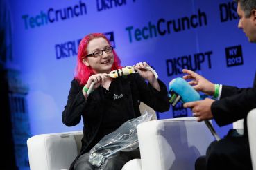 A woman with pink hair on a stage with a man holding an electronic device.