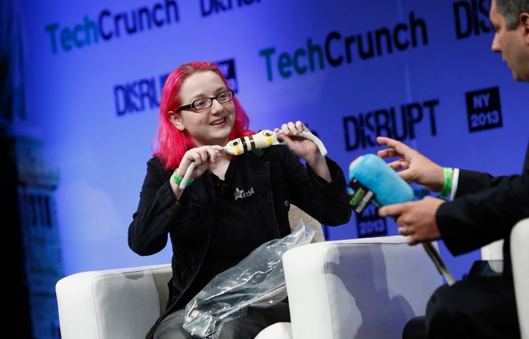 A woman with pink hair on a stage with a man holding an electronic device.