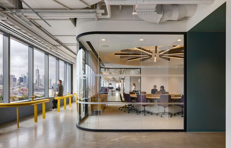 A walkway lined with yellow pedestals with an office on the right and a long window on the left.