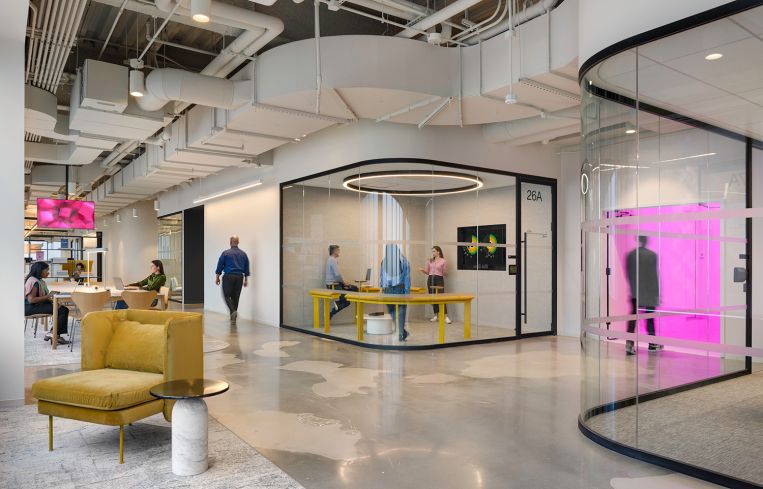 An open corridor in an office with a yellow armchair in the foreground.