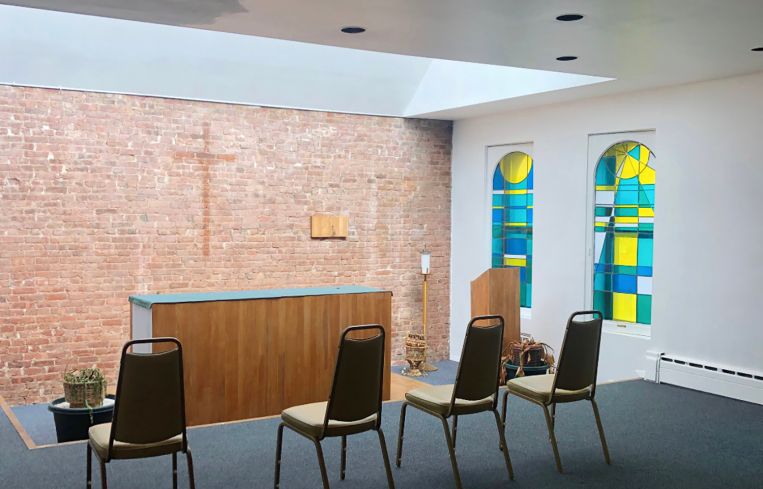 A row of chairs in front of an alter and a stained glass window.