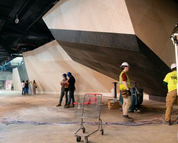 An unpainted climbing gym boulder and construction workers in hard hats.