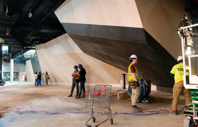 An unpainted climbing gym boulder and construction workers in hard hats.