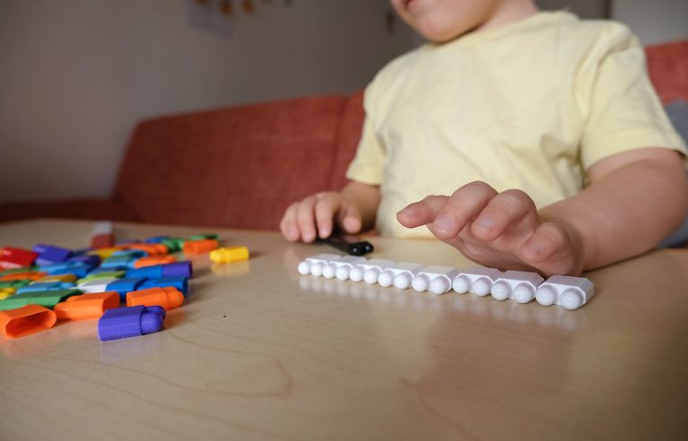 boy plays with multi-colored plastic blocks. Builds straight rows. A symptom of autism.