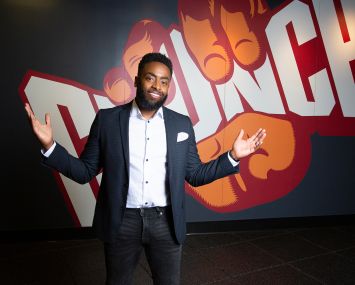 A man standing with arms outstretched in front of a sign that reads Crunch.