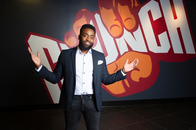 A man standing with arms outstretched in front of a sign that reads Crunch.