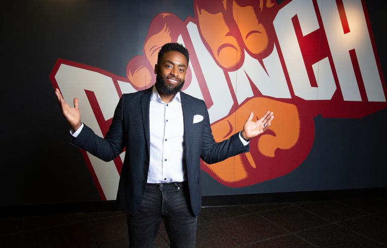 A man standing with arms outstretched in front of a sign that reads Crunch.