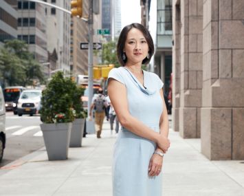 A young woman standing in a busy street with her hands folded.
