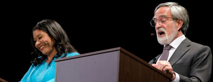 A woman and a man at podiums talking.